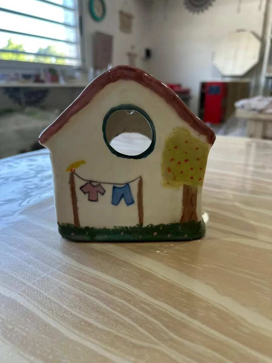Casita de cerámica pintada con un tendedero y un árbol