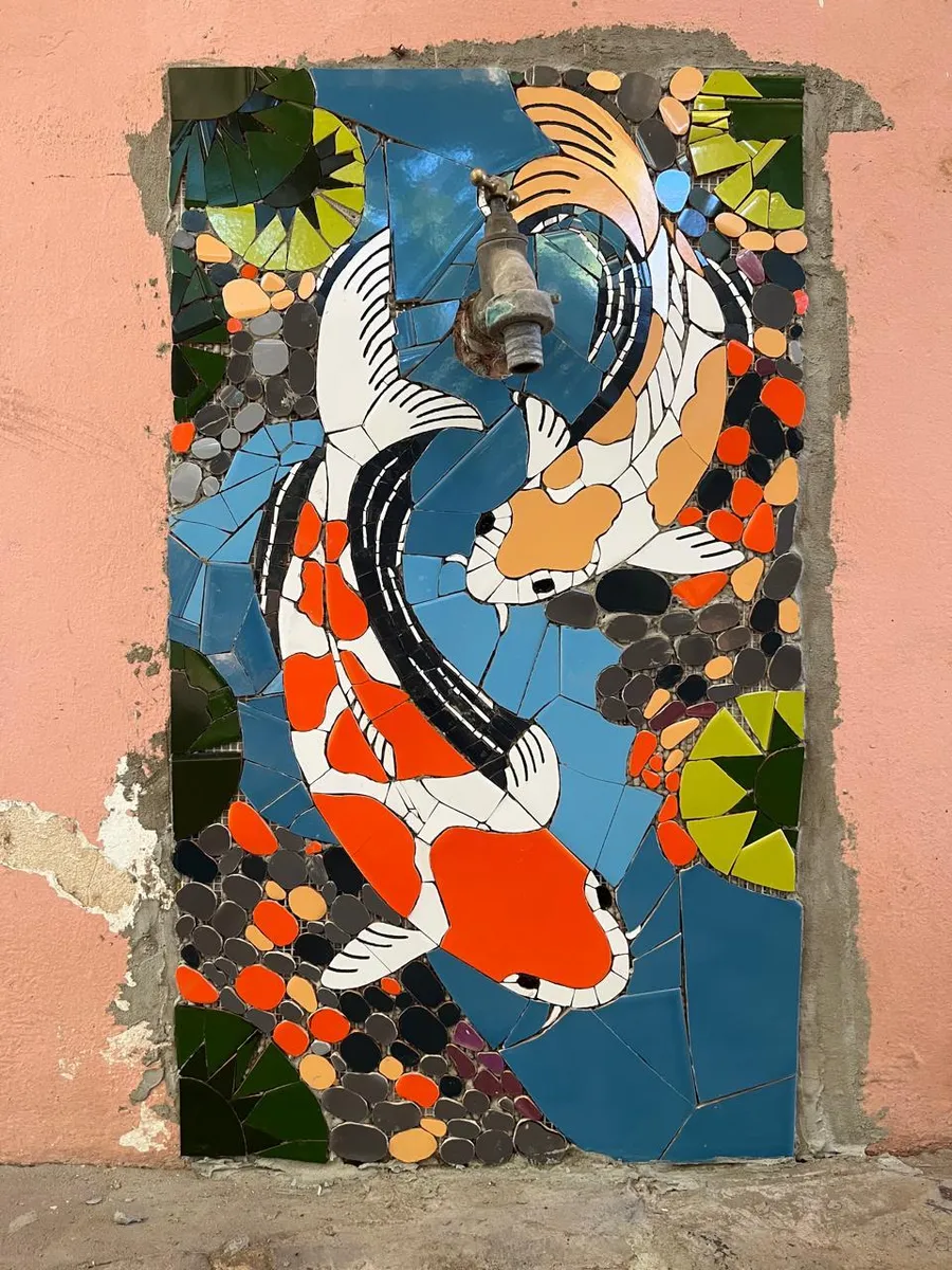 Mural de peces koi naranjas y blancos en mosaico sobre una pared