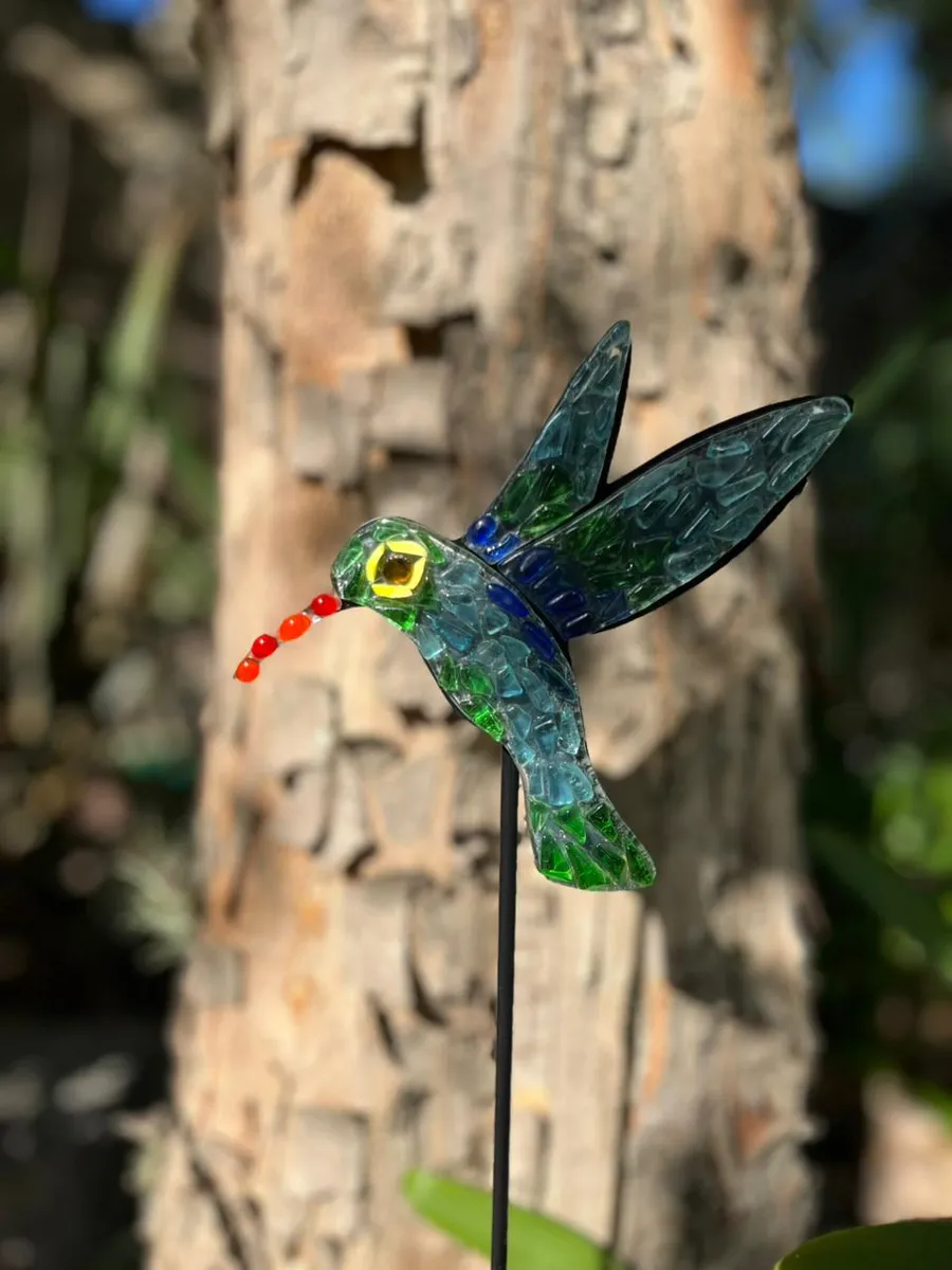 Colibrí de vitrofusión montado sobre una estaca, en el jardín